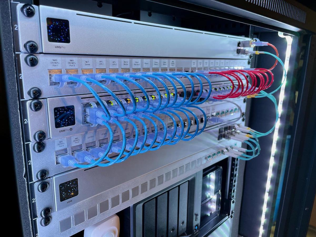 Server rack with network switches, neatly organized blue and red Ethernet cables, labeled ports, and LED status lights.